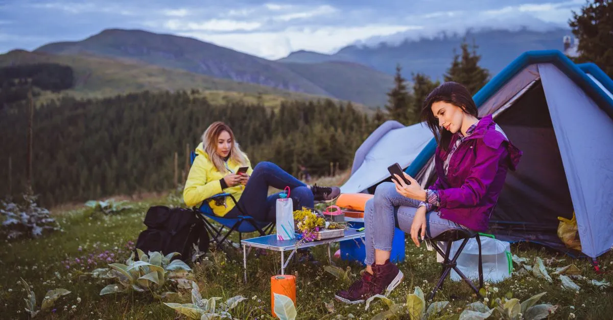 two women camping with phones in their hands